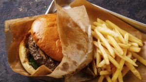 Burger with meat and French fries in aluminum tray on dark background
